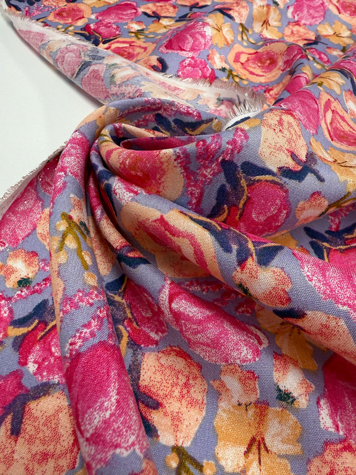 A close-up of Super Cheap Fabrics’ Designer Rayon - Botanic Crush (142cm) shows its vibrant pink, yellow, and orange floral print on purple. The softly draped fabric highlights its texture, making it a versatile choice for many projects.