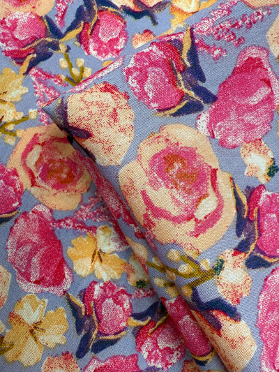 A close-up of Designer Rayon - Botanic Crush by Super Cheap Fabrics, featuring a colorful floral pattern with large pink, yellow, and cream flowers and green leaves on a light blue background—ideal for vibrant prints.