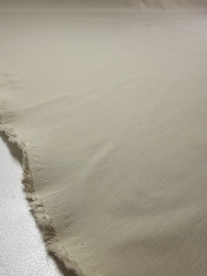 A close-up of Super Cheap Fabrics’ Cotton Bengaline - Bone White - 150cm shows its medium weight, slightly textured surface and frayed edge on the left.