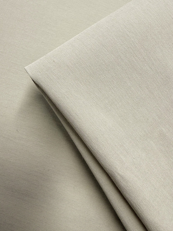 Two pieces of Cotton Bengaline - Bone White - 150cm by Super Cheap Fabrics are layered on a flat surface, with one piece folded. This medium weight fabric has a smooth texture and a subtle weave pattern.