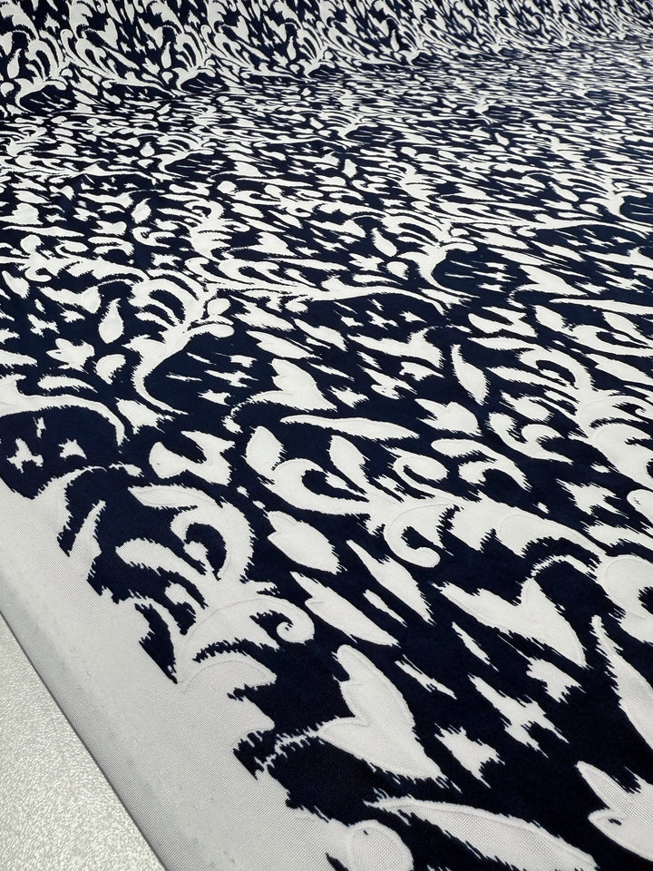 A close-up of Super Cheap Fabrics' Textured Lycra - Midnight Rococo (150cm) showcases a striking black and white abstract pattern, reminiscent of ornate prints, adding depth and visual interest.