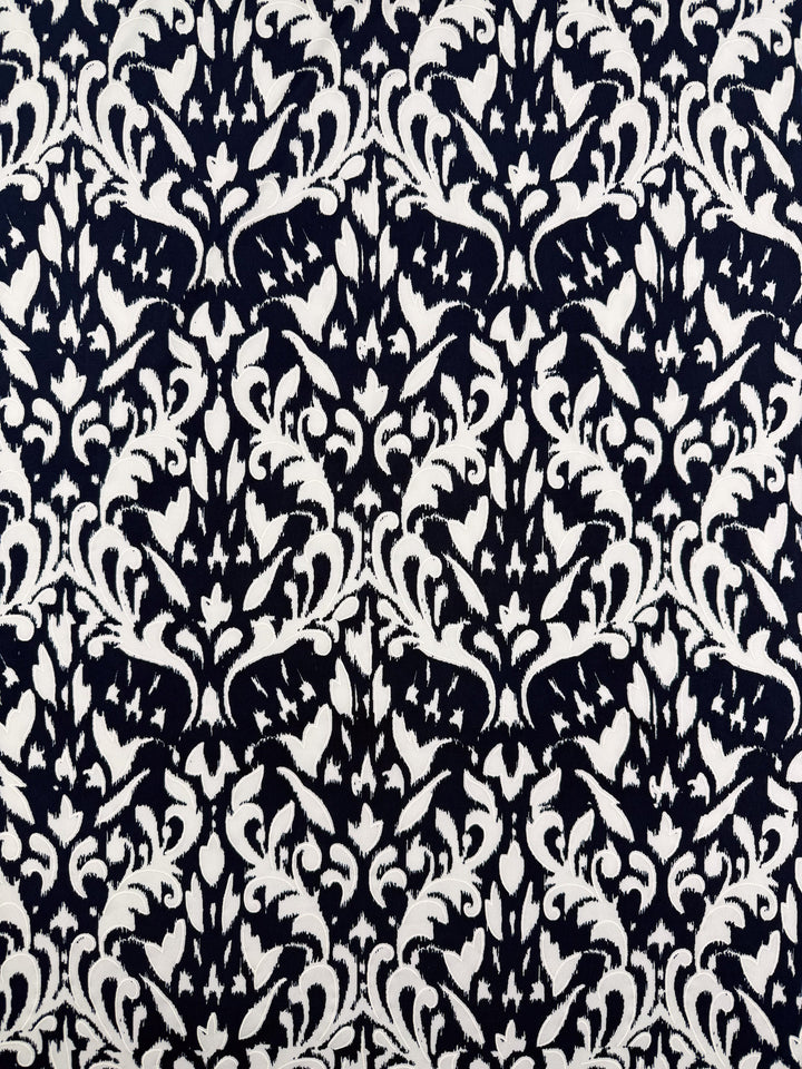 Super Cheap Fabrics' Textured Lycra - Midnight Rococo - 150cm features a black and white symmetrical abstract floral and leaf pattern on stretchy, comfortable lycra, creating a visually dense, ornamental design.