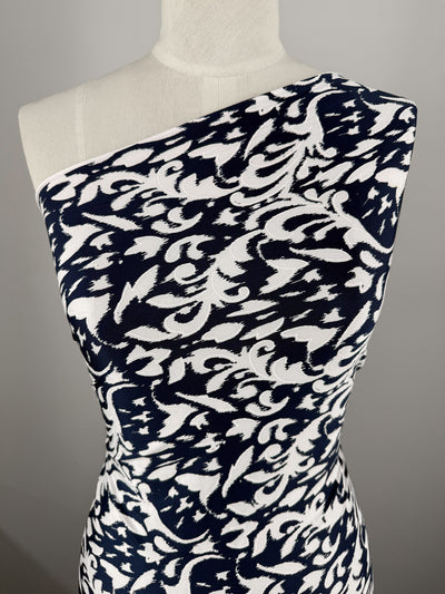 A dress form showcases Super Cheap Fabrics’ Textured Lycra - Midnight Rococo (150cm): an asymmetrical, one-shoulder garment in bold navy and white with swirling abstract designs on stretch fabric.