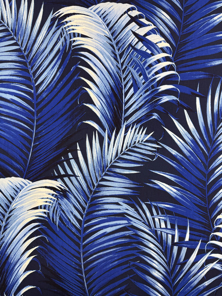 Close-up of Super Cheap Fabrics' Printed Lycra - Sapphire Jungle (150cm), showcasing bold blue and white palm leaves on a dark background—ideal for dynamic, tropical-inspired lycra or polyester spandex fabric creations.