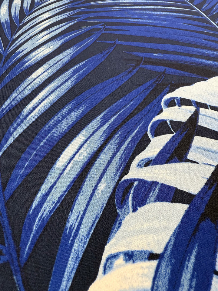 Close-up of Super Cheap Fabrics' Printed Lycra - Sapphire Jungle (150cm), showing its medium weight, blue and white tropical leaf pattern with overlapping leaves in various shades and detailed textures.