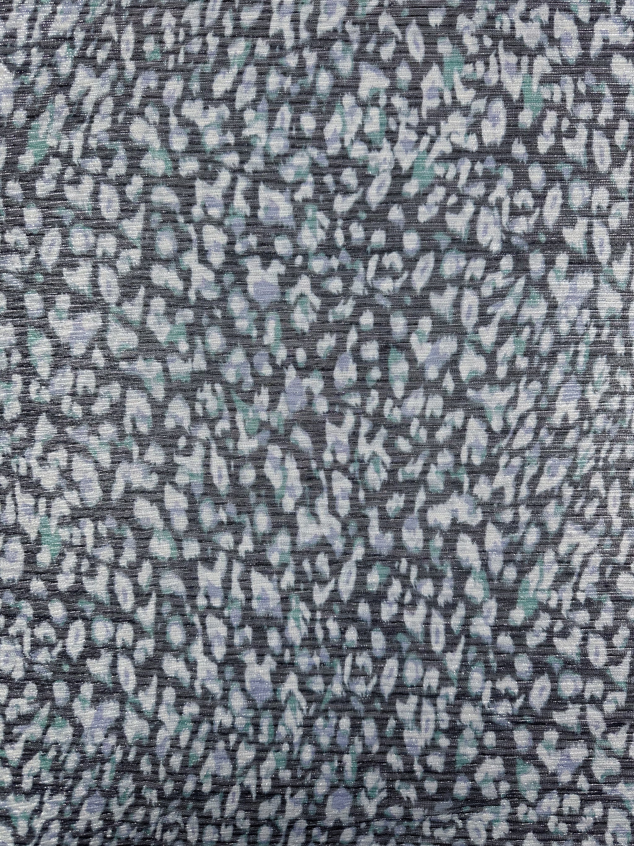 A detailed view of the Metallix Pleat - Ocean Leopard fabric by Super Cheap Fabrics reveals a lightweight polyester material with an abstract, textured pattern that resembles leopard spots. The background is gray, complemented by spots in shades of white, light blue, and navy for a repetitive design. The fabric measures 140cm in width.