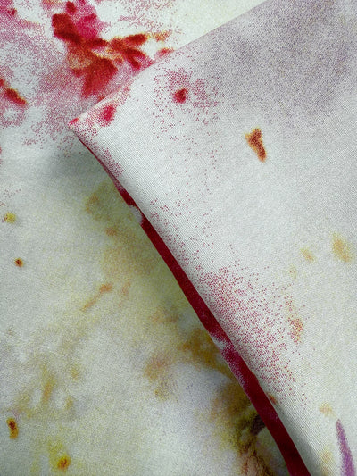 A close-up of Super Cheap Fabrics’ Designer Rayon - Aurora Bloom (143cm) shows soft, vibrant prints with red and yellow watercolor-like stains and a folded section revealing the fabric’s underside.