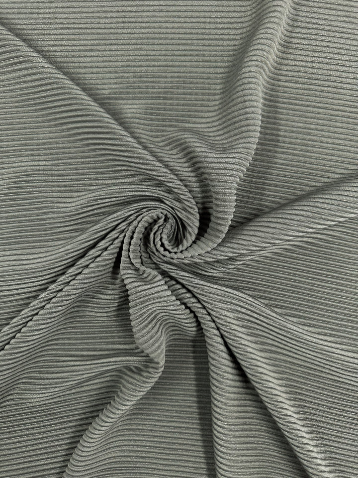 Close-up of Super Cheap Fabrics' Pleat in Pewter—140cm wide green corduroy with a swirling pattern. The lightweight fabric, folded in a spiral, highlights its ribbed design and soft pewter-colored appearance.