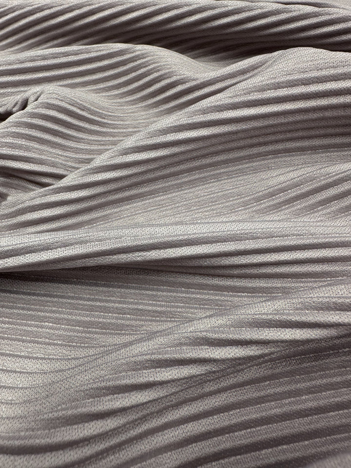 Close-up of "Pleat - Violet Ice - 140cm" by Super Cheap Fabrics: light gray ribbed polyester fabric with horizontal folds, creating a soft, flowing look reminiscent of violet ice.