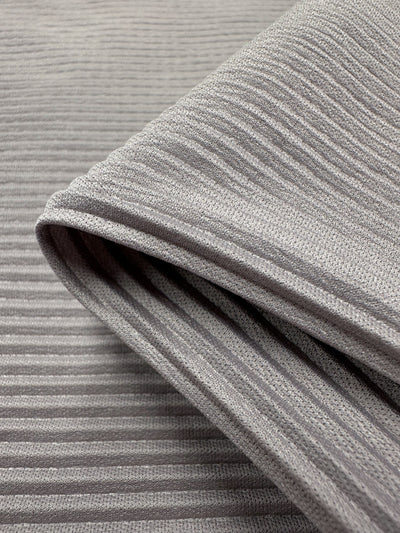 Close-up of folded gray ribbed polyester fabric shows horizontal ridges with an alternating pattern of raised and flat areas. Despite its soft, thick look, this lightweight fabric, Pleat - Violet Ice - 140cm by Super Cheap Fabrics, is suitable for warm clothing or upholstery.