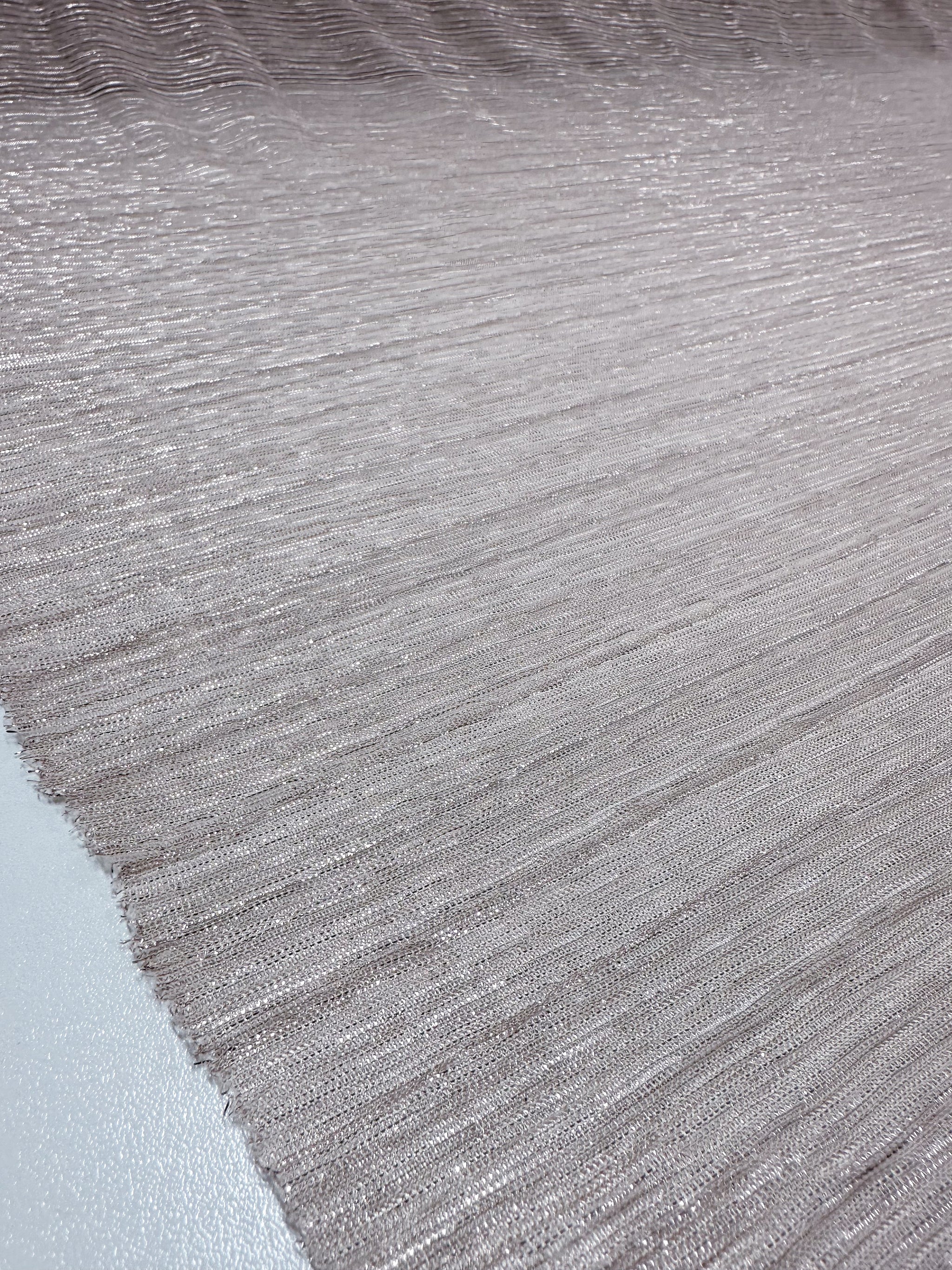 A close-up of the Metallix Pleat - Blush fabric from Super Cheap Fabrics showcases its textured, light brown appearance with subtle horizontal ridges. The lightweight polyester surface is smooth and slightly reflective, providing an elegant sheen across the 140cm material.