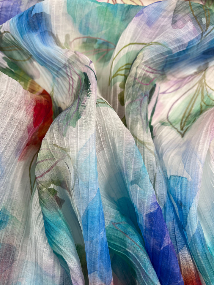 Close-up of "Textured Tencel - Dream Flor - 136cm" from Super Cheap Fabrics, a colorful sheer fabric with a floral pattern. This sustainable material features crinkled textures in shades of blue, green, red, and purple.