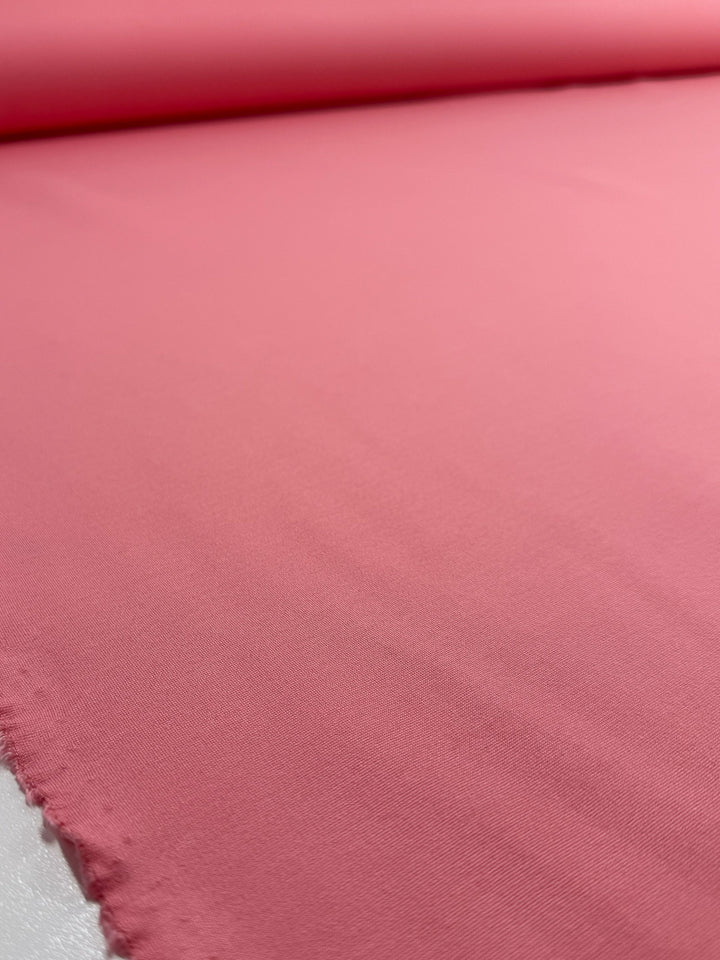 A close-up of Super Cheap Fabrics' Milano Ponte - Flamingo Pink (160cm), showing its smooth texture and a slightly frayed edge on the left, spread across a flat surface.