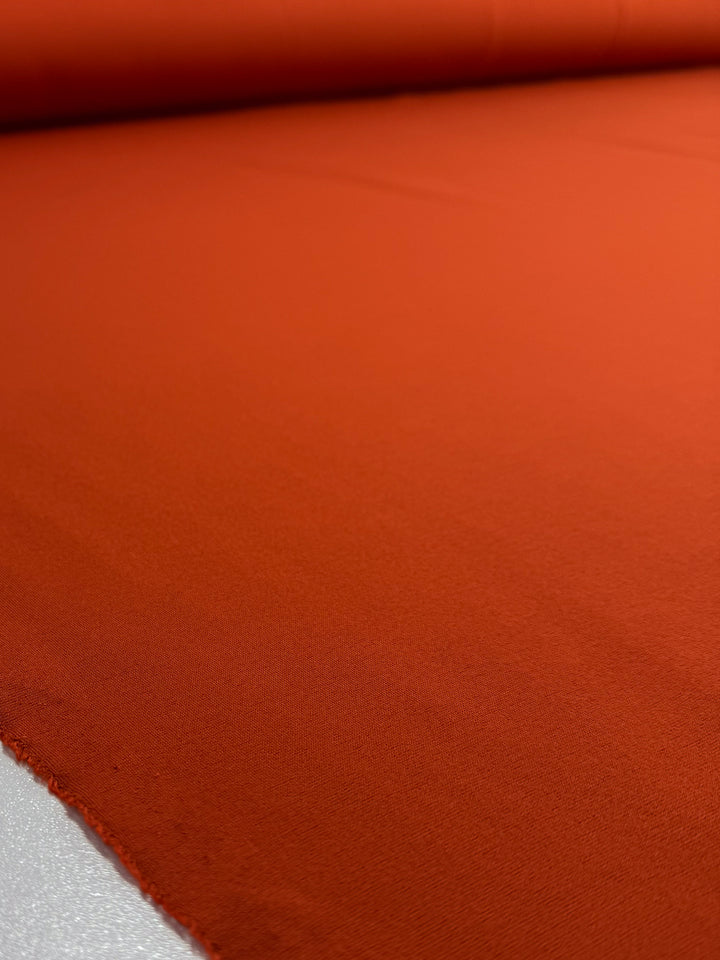 A close-up of Super Cheap Fabrics’ Milano Ponte - Chili - 160cm roll shows its vibrant orange color and finely textured, smooth surface spread out for detail.