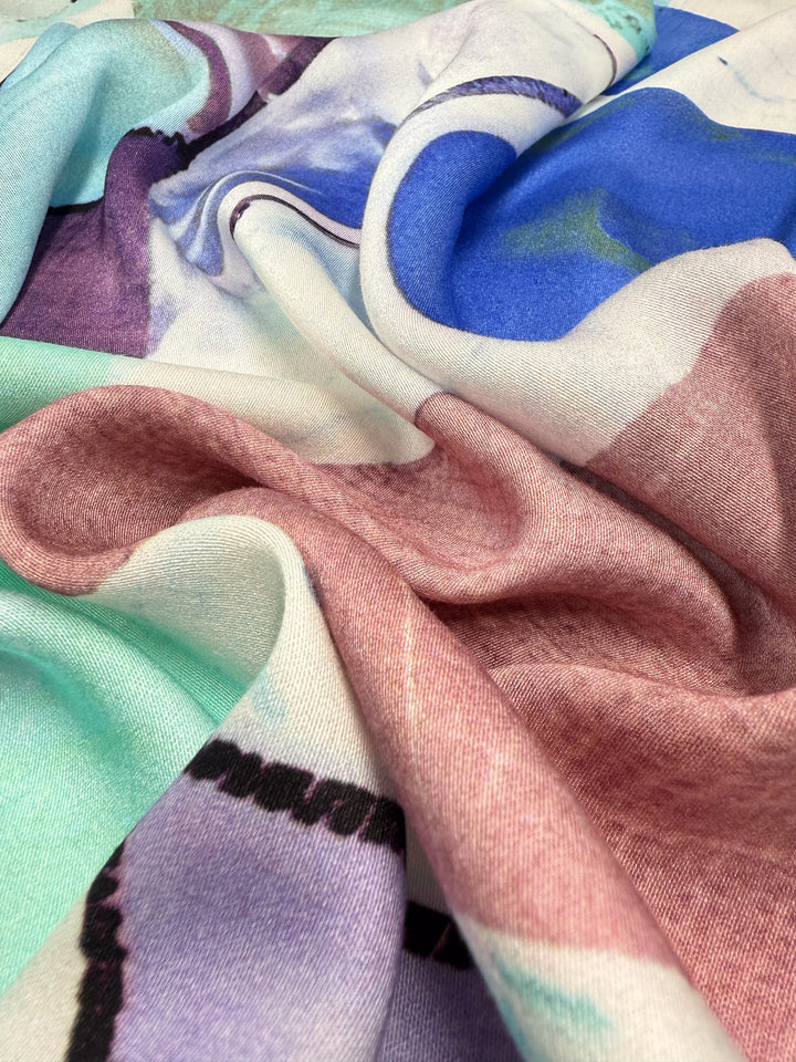 A close-up of Mercerised Rayon - Mid Mod Mirage (150cm) by Super Cheap Fabrics, a lightweight, breathable rayon with a smooth, flowing abstract pattern in pastel pink, blue, mint green, and white.