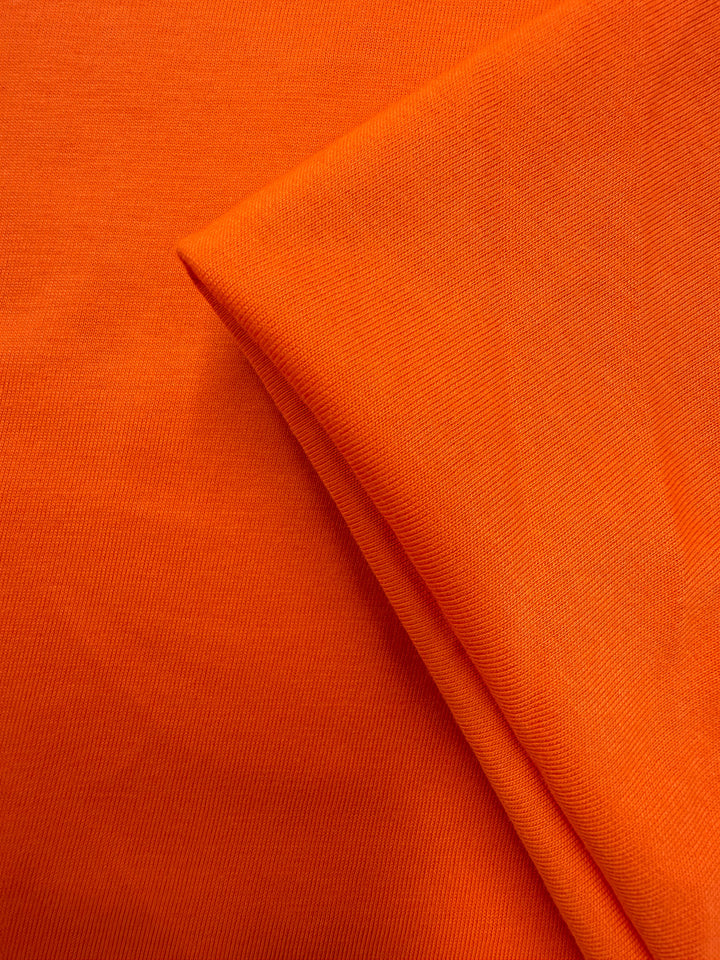 Close-up of Super Cheap Fabrics' Cotton Jersey - Mandarin Orange - 165cm, showing a neatly folded section that reveals its vibrant color, fine texture, and lightweight weave.