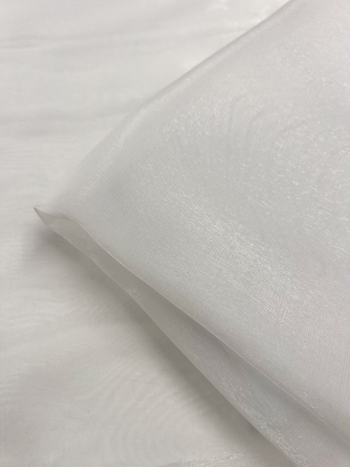 A close-up of Super Cheap Fabrics’ Silk Mousseline - Alabaster - 135cm, a sheer, extra light silk with a slightly shiny, translucent texture, neatly folded on a matching white background.