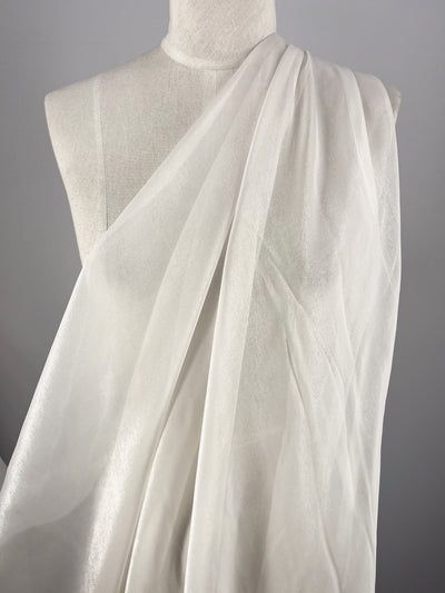 Super Cheap Fabrics’ Silk Mousseline - Alabaster - 135cm, a white, extra lightweight sheer silk, is draped over a dress form to create soft flowing folds that reveal its texture and subtle translucence against a plain gray backdrop.