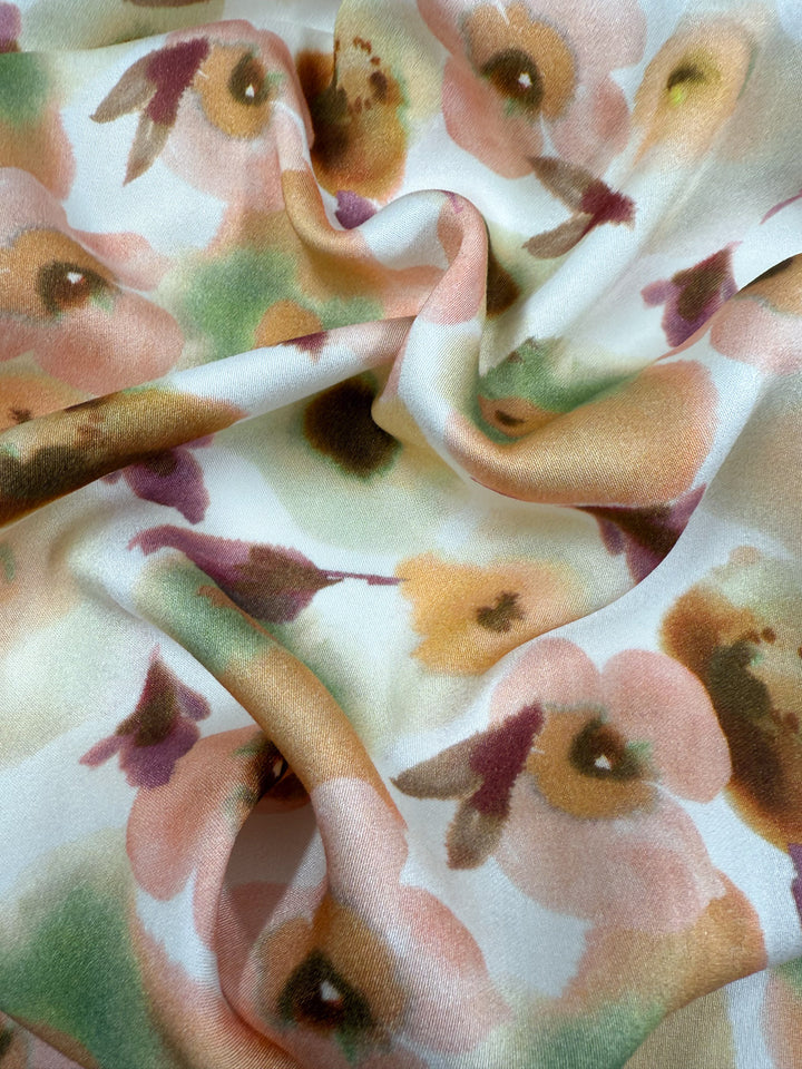 Super Cheap Fabrics' Mercerised Rayon - Blushed Camellia (150cm) is a soft, lightweight rayon with a watercolor floral print in pink, peach, green, and brown on white. The smooth fabric drapes beautifully for textured, flowing projects.