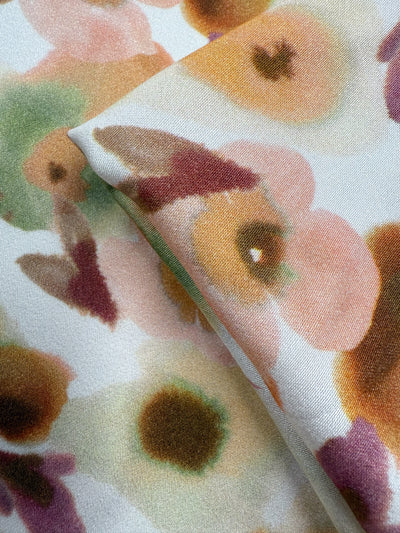 A close-up of Super Cheap Fabrics’ Mercerised Rayon - Blushed Camellia (150cm), featuring a lightweight fabric with a watercolor floral pattern in soft pink, green, brown, and yellow on white.