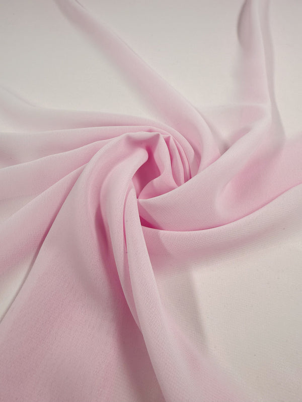 The Hi-Multi Chiffon - Cradle Pink - 150cm from Super Cheap Fabrics is a light pink sheer polyester, artfully spiraled on a white surface to showcase its soft folds and delicate texture.