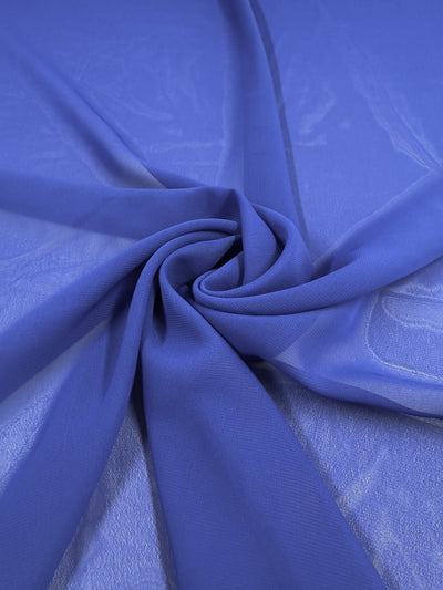 A close-up of Super Cheap Fabrics’ Hi-Multi Chiffon – Dazzling Blue (150cm) arranged in gentle folds and spiral on a flat surface, highlighting its soft texture and delicate transparency.