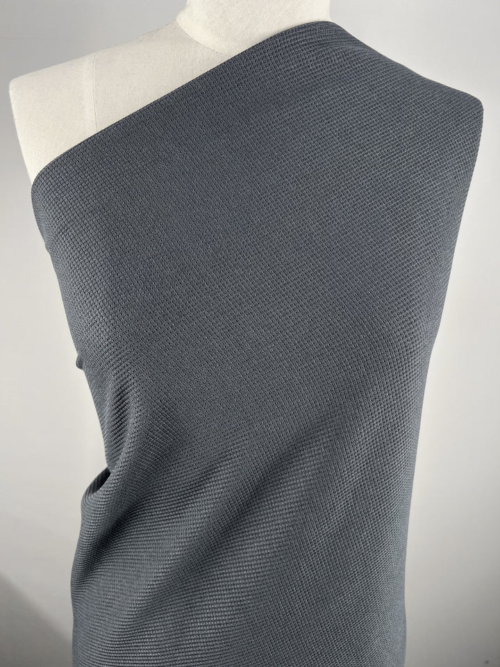 A mannequin showcases Super Cheap Fabrics’ Waffle Knit - Charcoal - 170cm, draped over one shoulder with a diagonal neckline, set against a plain light background.