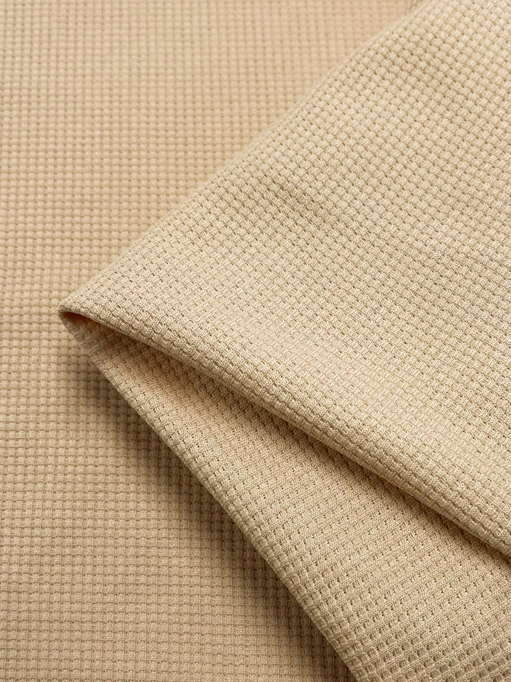 The Waffle Knit - Sun Kiss from Super Cheap Fabrics features a beige waffle texture with a grid-like pattern of small, raised squares. Its soft, three-dimensional appearance adds depth and texture to the fabric surface. Width: 170cm.