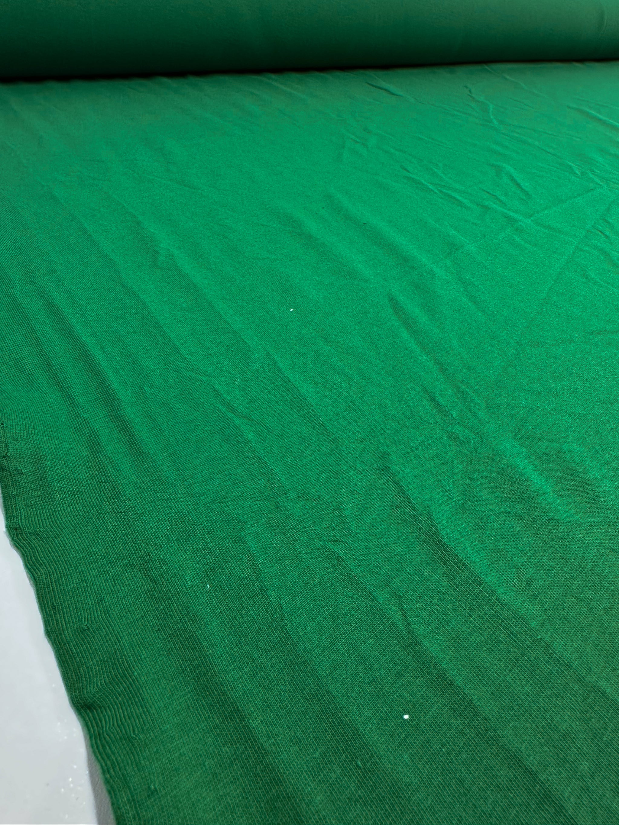 A close-up view of Super Cheap Fabrics' Cotton Jersey in Abundant Green, width 165cm, showcases its texture and subtle wrinkles.