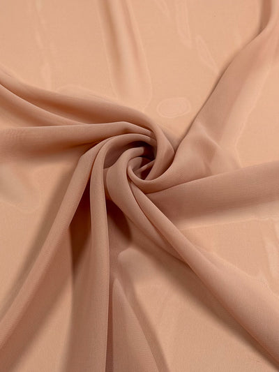 A close-up of Super Cheap Fabrics' Hi-Multi Chiffon in Pink Sand (150cm), showing its lightweight, sheer texture arranged in soft, flowing folds with a spiral twist at the center.