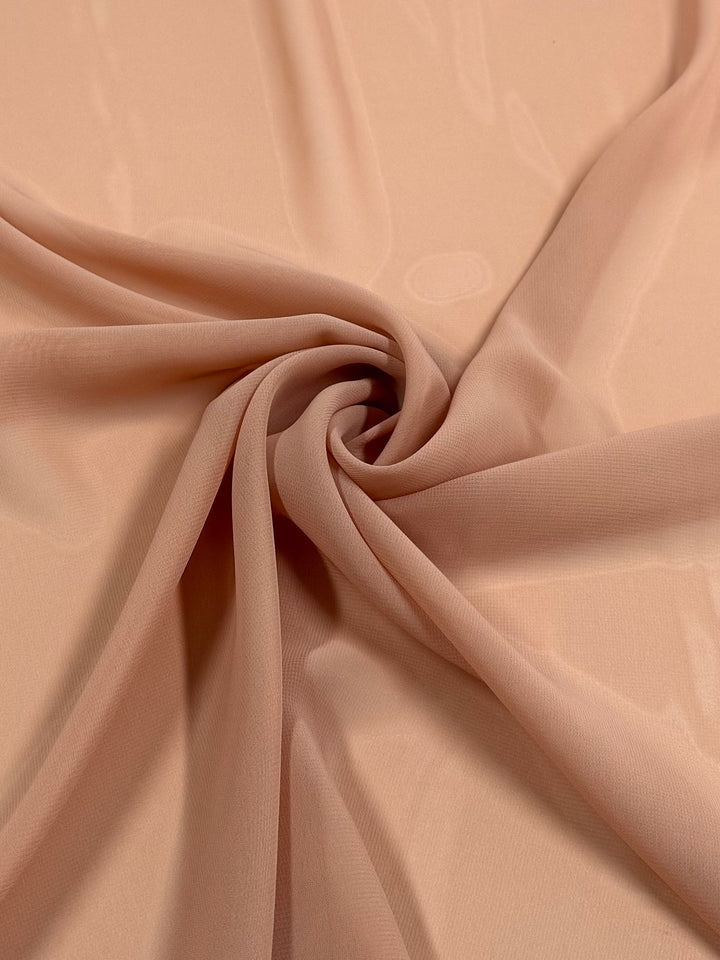 A close-up of Super Cheap Fabrics' Hi-Multi Chiffon in Pink Sand (150cm), showing its lightweight, sheer texture arranged in soft, flowing folds with a spiral twist at the center.