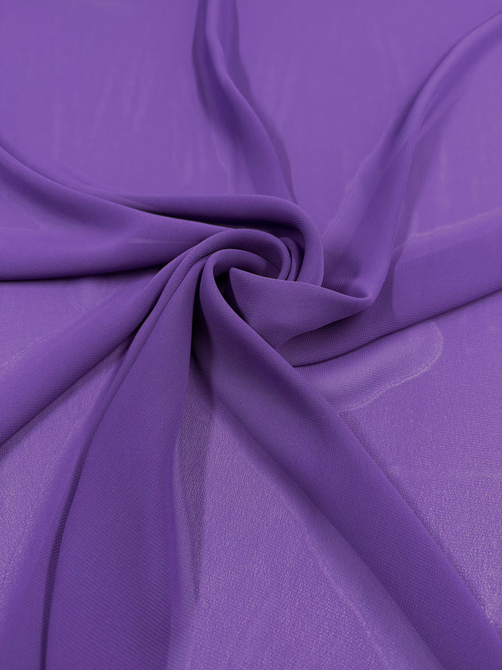 Hi-Multi Chiffon - Passion Flower by Super Cheap Fabrics (150cm) features sheer purple lightweight fabric draped in soft folds, forming a swirling spiral design at the center on a smooth backdrop.