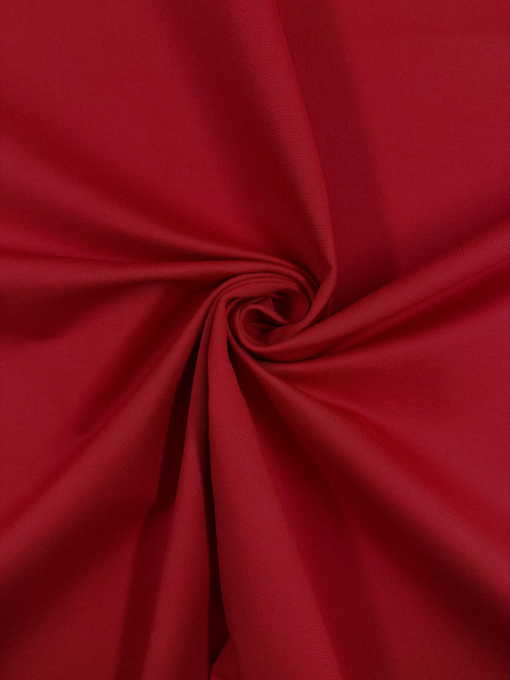 A close-up of Milano Ponte - True Red by Super Cheap Fabrics, 160cm wide, twisted to display its smooth texture, vibrant red color, and 4-way stretch qualities.