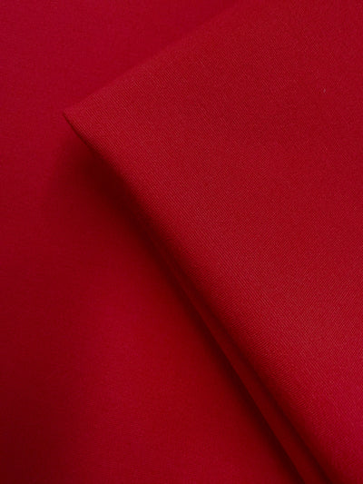 Close-up of two pieces of Super Cheap Fabrics' Milano Ponte - True Red (160cm): one piece lies flat, the other folded on top, highlighting the fabric’s smooth and slightly textured surface.