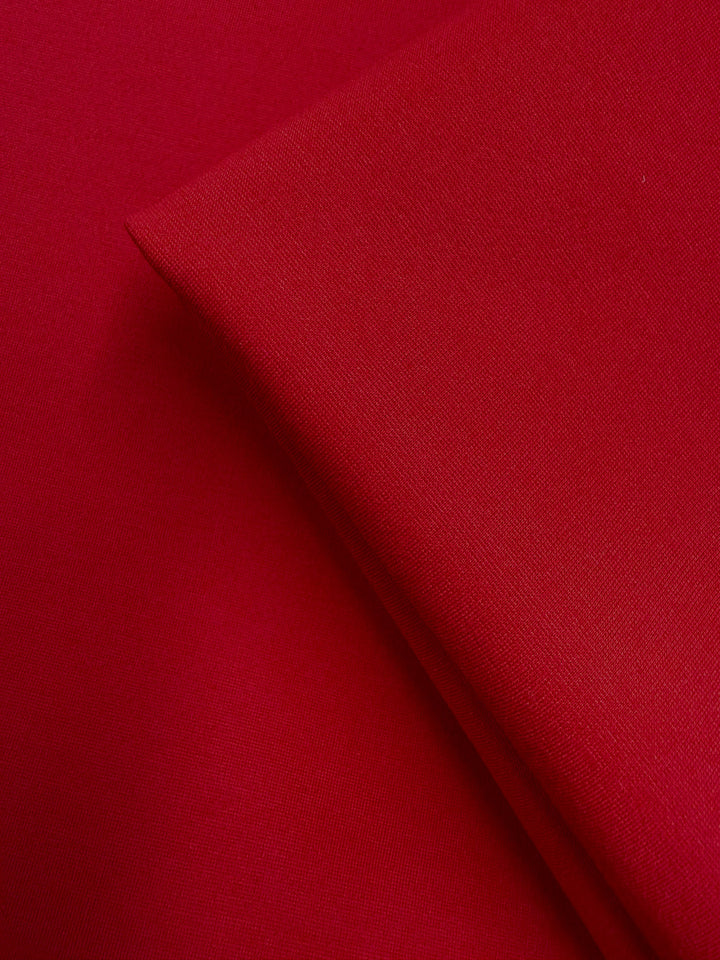 Close-up of two pieces of Super Cheap Fabrics' Milano Ponte - True Red (160cm): one piece lies flat, the other folded on top, highlighting the fabric’s smooth and slightly textured surface.