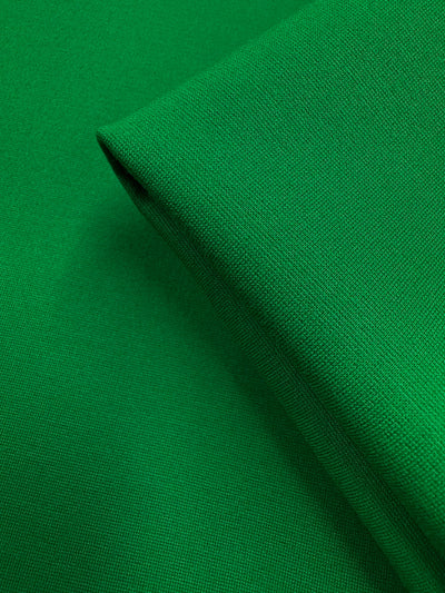 A close-up of Super Cheap Fabrics' Milano Ponte - Jolly Green (160cm) reveals its smooth, heavy-weight, woven texture and vibrant solid color with a neatly folded edge.