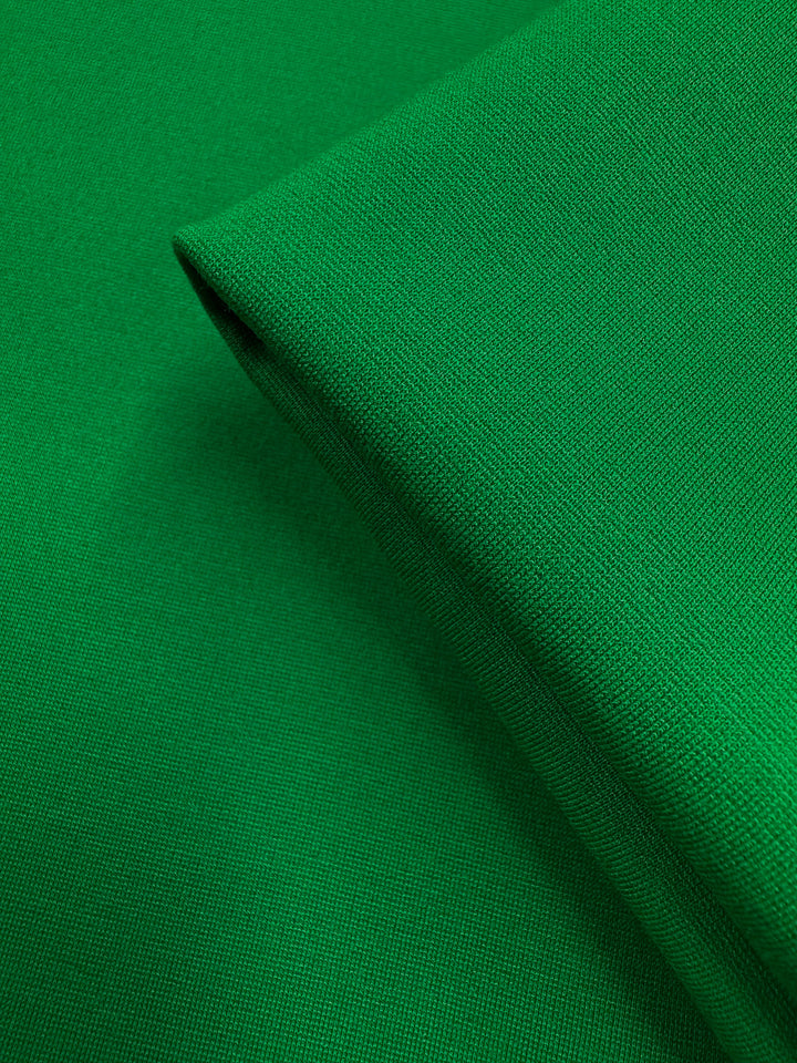 A close-up of Super Cheap Fabrics' Milano Ponte - Jolly Green (160cm) reveals its smooth, heavy-weight, woven texture and vibrant solid color with a neatly folded edge.