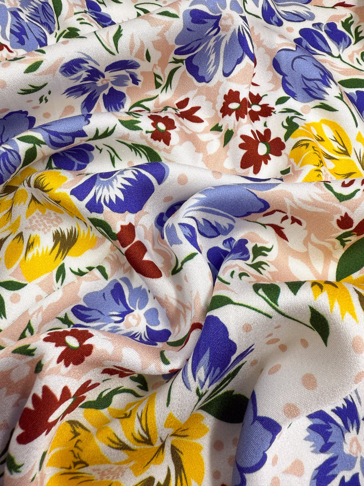 Close-up of Super Cheap Fabrics’ Mercerised Rayon - Spring Bouquet (150cm), featuring a colorful floral pattern with blue, yellow, and red flowers with green leaves on white. This lightweight fabric offers both style and comfort.