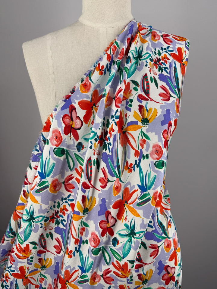 A dress form displays Super Cheap Fabrics’ Mercerised Rayon - Tropical Brushstroke, a vibrant, breathable fabric with a colorful abstract floral pattern in red, orange, pink, purple, green, and blue on a light background.