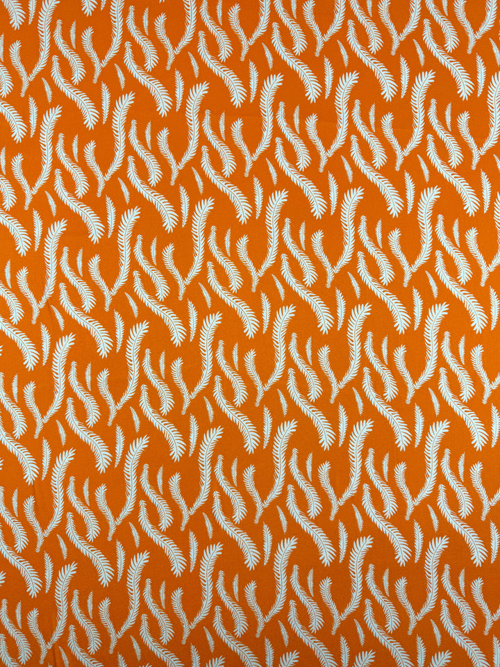 Super Cheap Fabrics’ Mercerised Rayon - Citrus Flow - 150cm features lightweight orange rayon with a repeating white fern motif, creating a dynamic, flowing effect and beautiful drape across the bright background.
