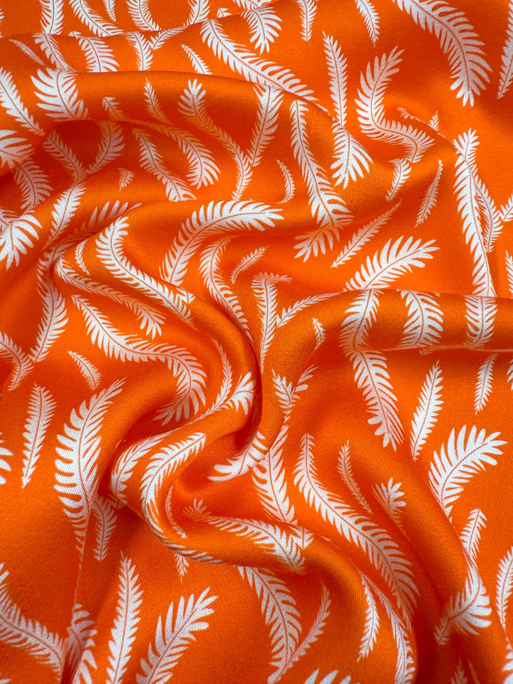 Super Cheap Fabrics’ Mercerised Rayon - Citrus Flow (150cm) is a vibrant orange, lightweight fabric with swirling patterns and white palm leaf motifs. The rayon drapes softly, adding gentle folds and textured style to your creations.