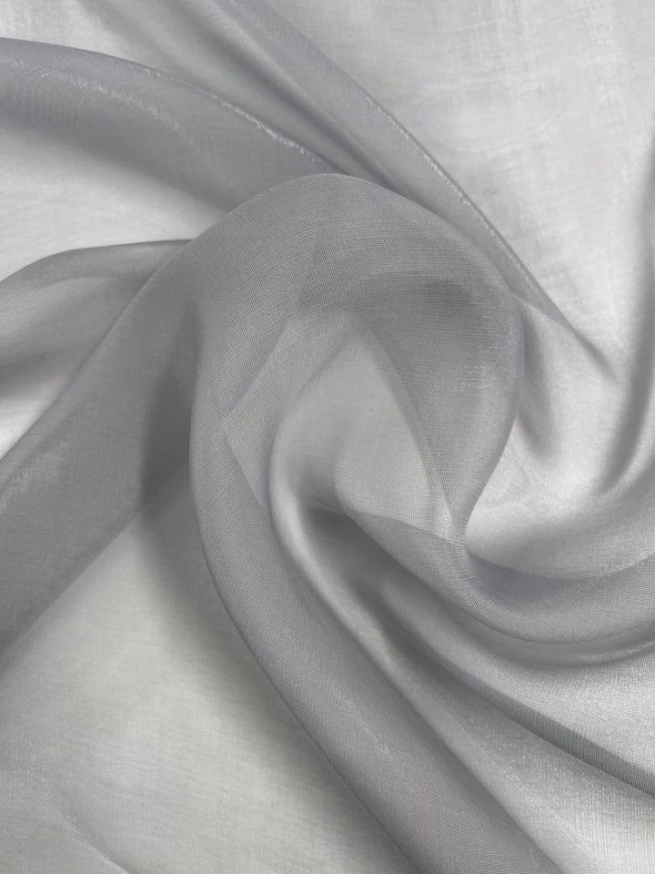 Close-up of Super Cheap Fabrics' Silk Mousseline - Moonbeam - 140cm, draped in sheer gray folds highlighting its smooth, translucent texture. It softly catches light to produce a metallic shimmer with subtle tonal variations.