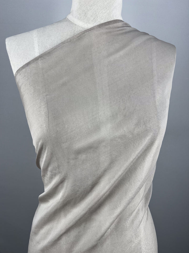 Silk Mousseline - Marble by Super Cheap Fabrics is a light gray, extra lightweight, semi-sheer silk with a subtle metallic shimmer shown draped diagonally over a white dress form against a plain gray background. Width: 140cm.