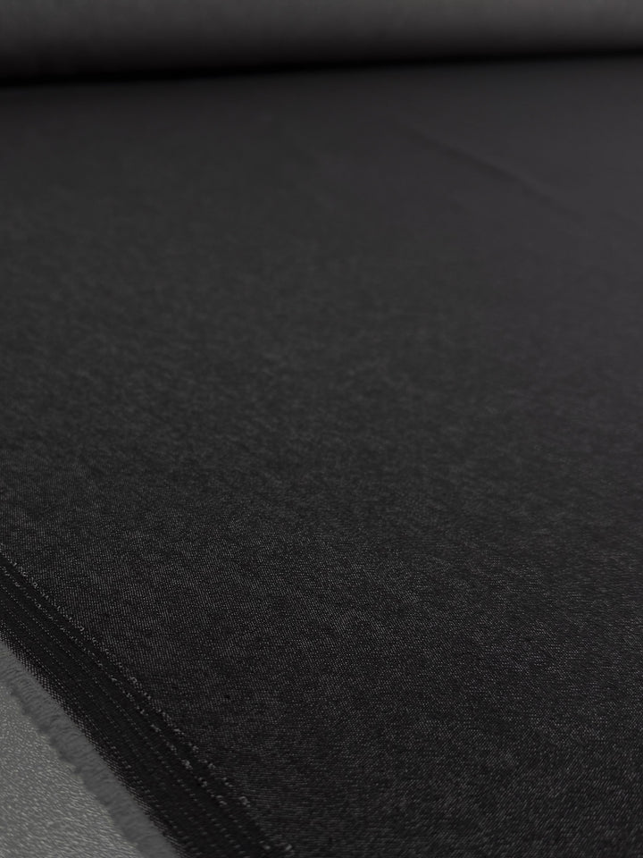 A close-up of Super Cheap Fabrics' Denim - Black - 150cm shows the fabric’s smooth texture and even solid black color as it is spread out on a flat surface.