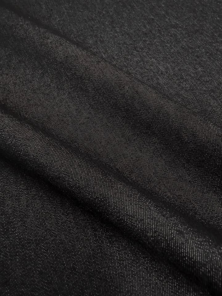 A close-up of Denim - Black - 150cm by Super Cheap Fabrics shows visible diagonal weaving and soft folds, highlighting the rich texture and structure of premium cotton denim.