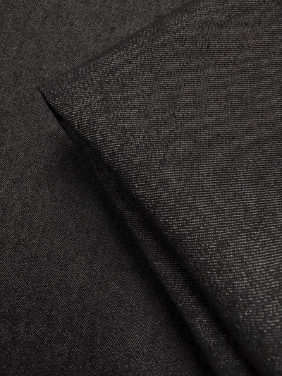 A close-up of Super Cheap Fabrics’ Denim - Black - 150cm shows the fine weave and subtle sheen of this angled, folded black denim fabric.