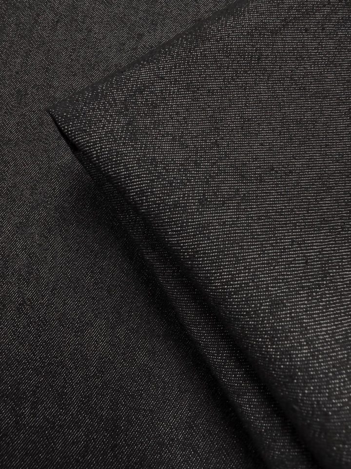 A close-up of Super Cheap Fabrics’ Denim - Black - 150cm shows the fine weave and subtle sheen of this angled, folded black denim fabric.