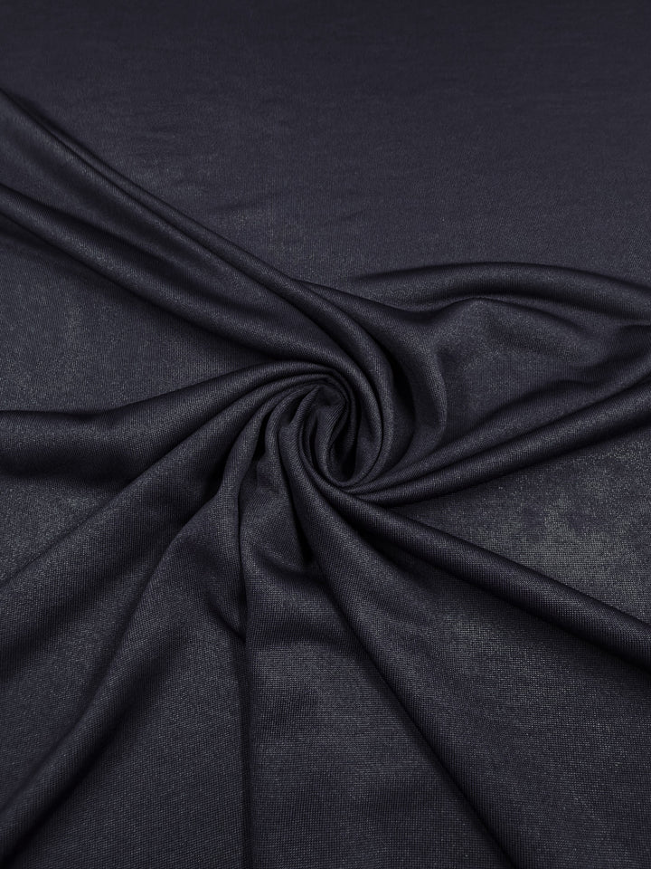 A close-up of Super Cheap Fabrics' Knit Lining - Dark Navy - 160cm, arranged in gentle folds to form a spiral and showcase the lightweight fabric's smooth, slightly shiny texture.