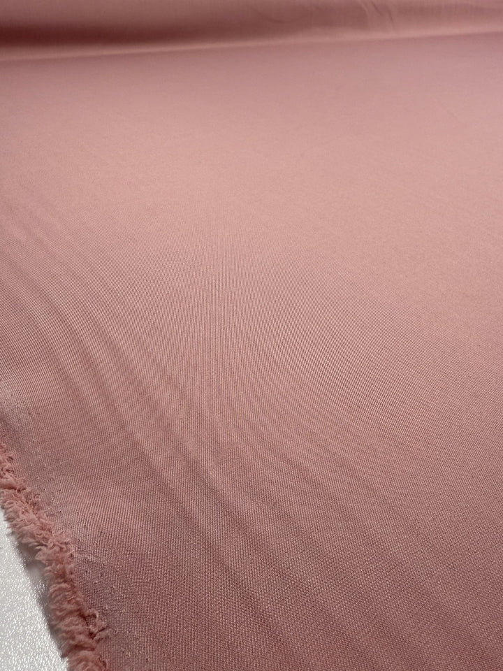 A close-up of Super Cheap Fabrics' Liquid Twill in Misty Rose (150cm), showing its soft, evenly colored surface, subtle texture, and a slightly frayed edge along the left.