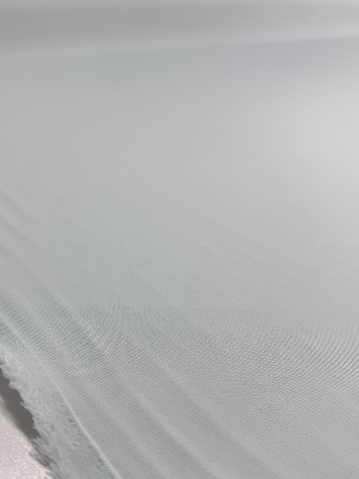A close-up of Super Cheap Fabrics’ Liquid Twill - Murmur (150cm), featuring its light grey, smooth yet slightly textured surface with visible edges and soft folds.
